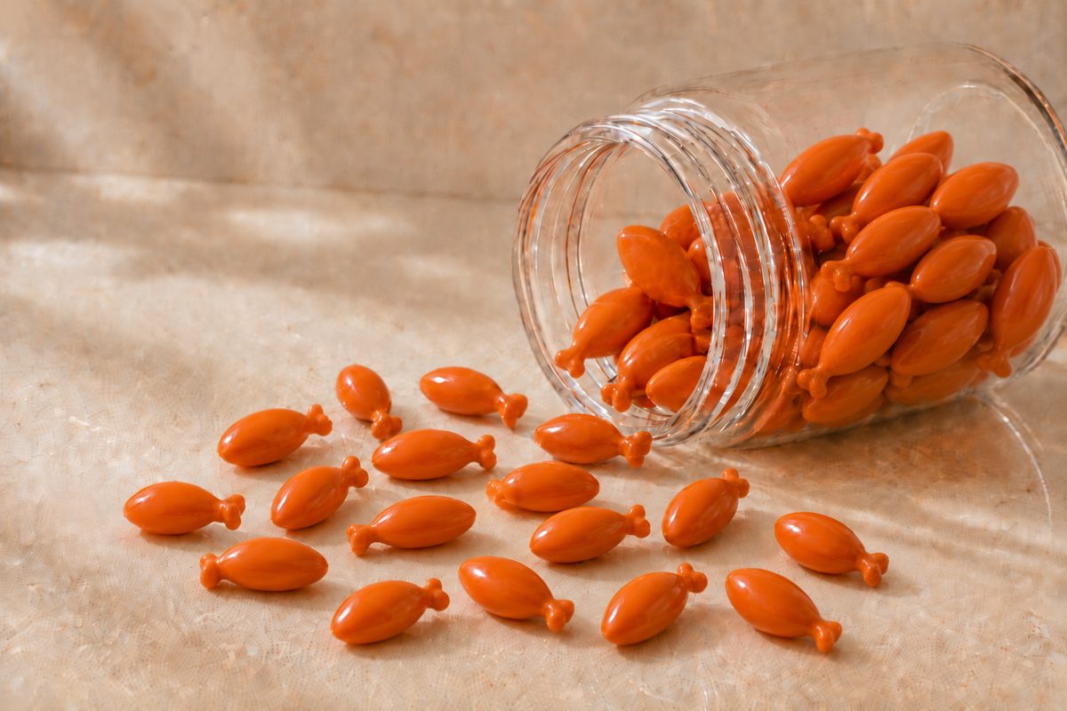 Orange fish-shaped PHPS chewable softgels spilling from a glass jar &mdash; confectionery format gel candy with astaxanthin or DHA fill