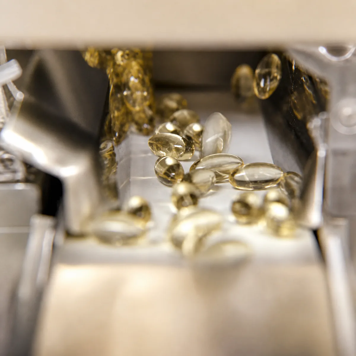 Plant softgel encapsulation machine — golden softgels emerging from die rolls in pharmaceutical-grade manufacturing equipment